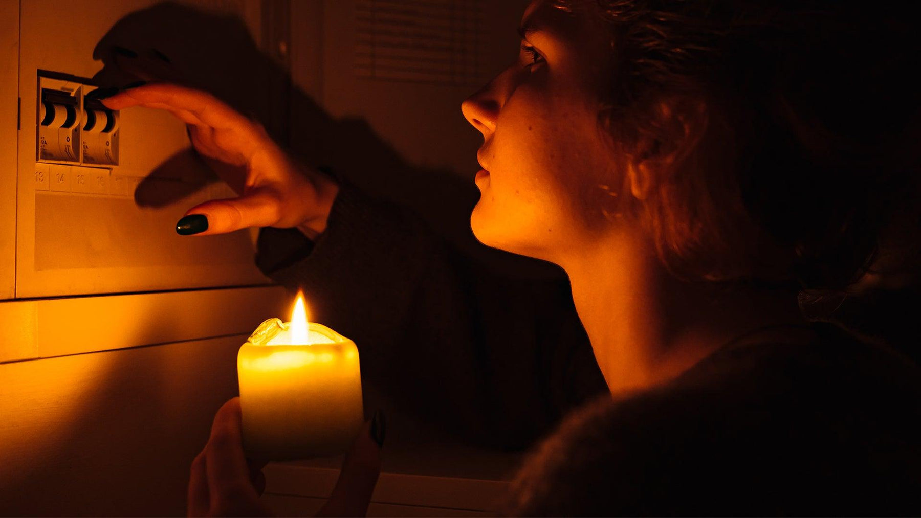Woman holding candle near electrical panel during power outage loadshedding