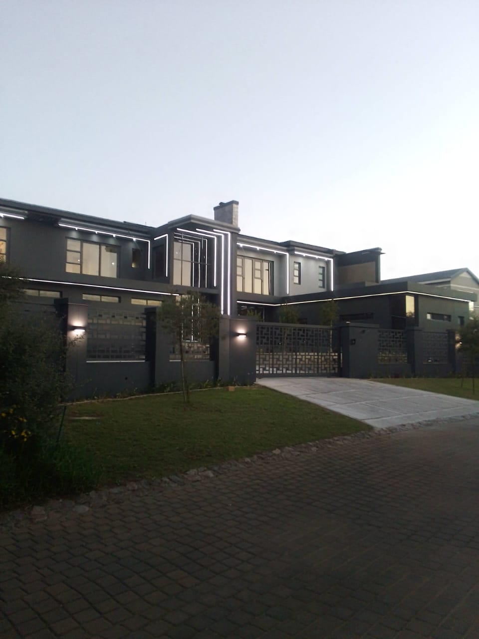 Modern building exterior with bing light led strip lights and a driveway and grass area at dusk.